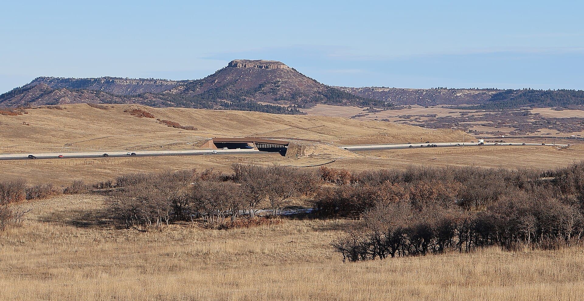 I-25 Greenland Wildlife Overpass spanning Interstate 25 near Larkspur and Monument, Douglas County, Colorado, with grassland approaches and a mesa beyond. Photo: Jeffrey Beall, via Wikimedia Commons (CC BY 4.0). Source page: https://commons.wikimedia.org/wiki/File:I-25_Greenland_Wildlife_Overpass-1.JPG