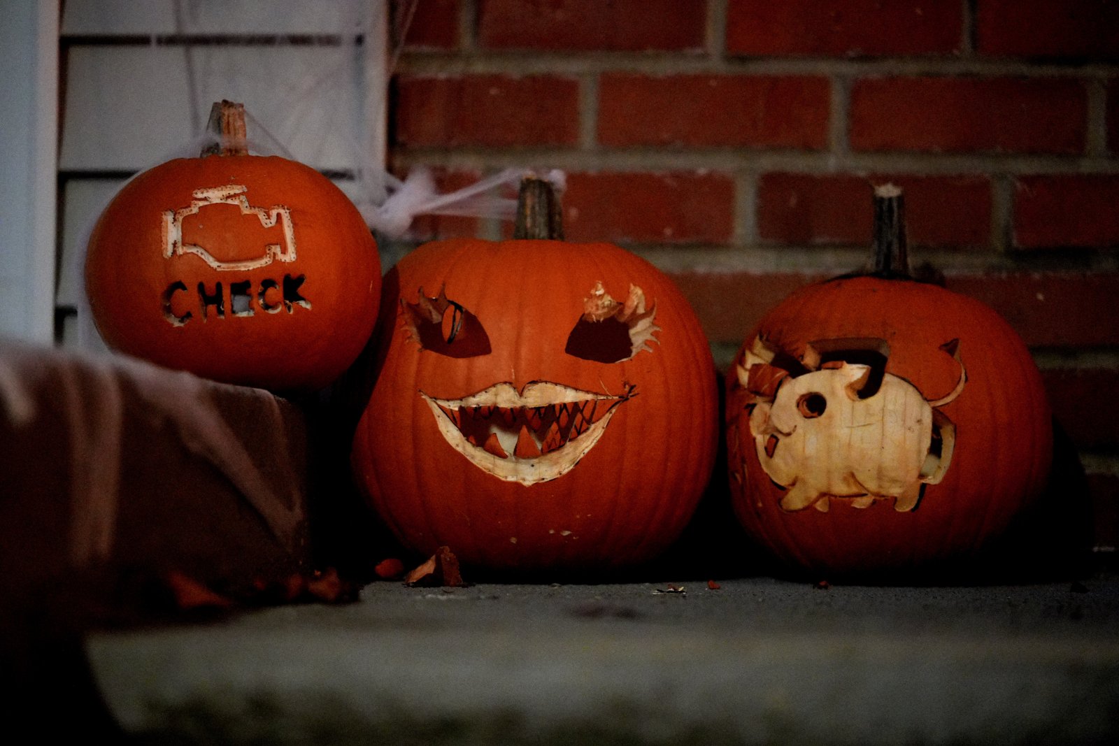 Three carved jack-o'-lanterns sit on a concrete porch step against a red brick wall.